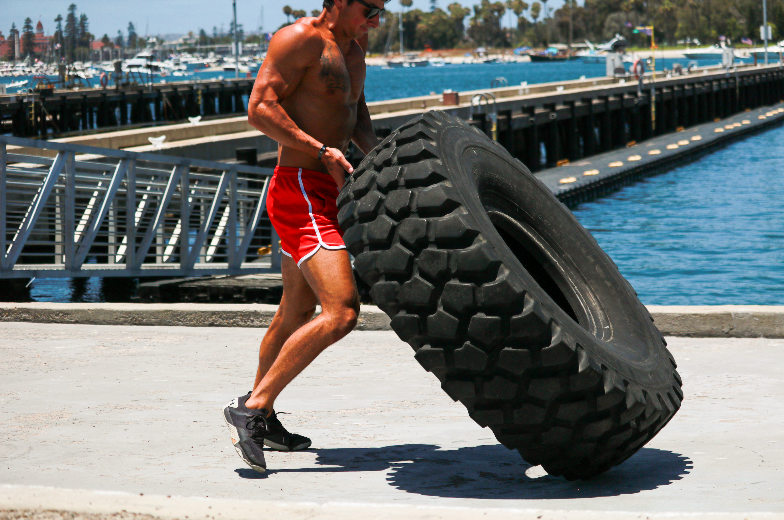 Fit man flipping big tire over while training near water